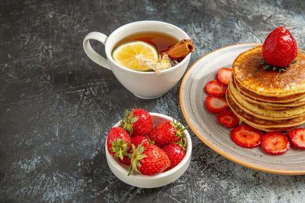 Vue avant de délicieuses crêpes avec du thé et des fruits sur la surface légère gâteau aux fruits sucré