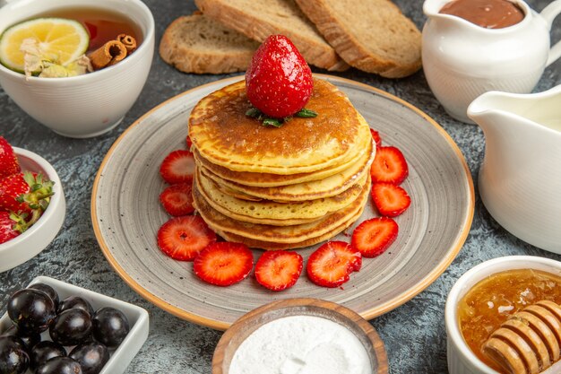 Vue avant de délicieuses crêpes avec du thé et des fruits sur la surface légère gâteau aux fruits sucré