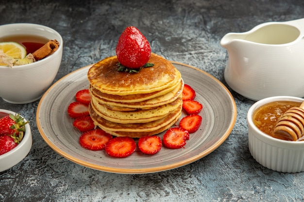 Vue avant de délicieuses crêpes avec des fruits et du miel sur une surface légère de fruits gâteau sucré