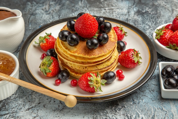 Vue avant de délicieuses crêpes avec des fruits frais et du miel sur une surface légère gâteau aux fruits sucré