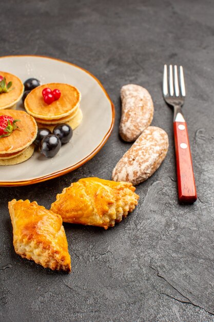 Vue avant de délicieuses crêpes avec des gâteaux et des fruits sur la surface sombre gâteau sucré aux fruits