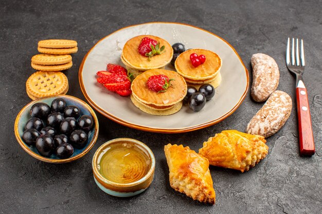 Vue avant de délicieuses crêpes avec des gâteaux et des fruits sur la surface sombre gâteau sucré aux fruits