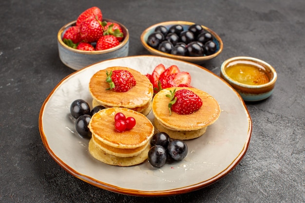 Vue avant de délicieuses crêpes peu formées avec des fruits sur la surface grise gâteau aux fruits tarte