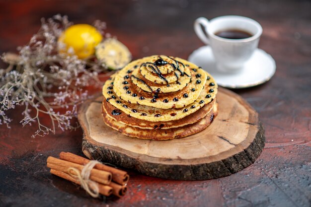 Vue avant de délicieuses crêpes sucrées avec du thé sur fond sombre