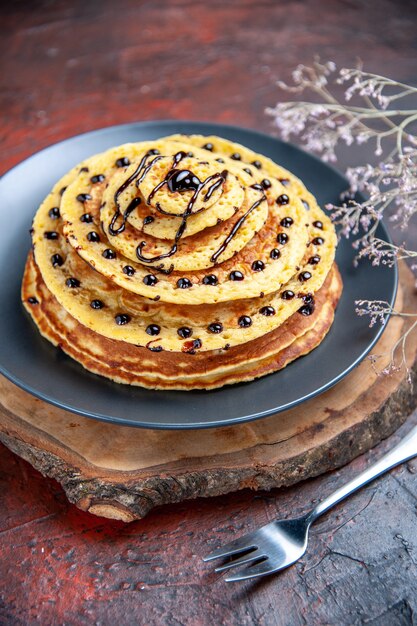 Vue avant de délicieuses crêpes sucrées avec glaçage au chocolat sur fond sombre