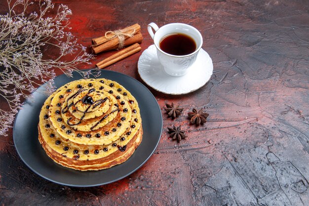 Vue avant de délicieuses crêpes sucrées avec tasse de thé sur fond sombre gâteau dessert sucré lait