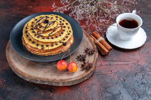 Photo gratuite vue avant de délicieuses crêpes sucrées avec tasse de thé sur fond sombre