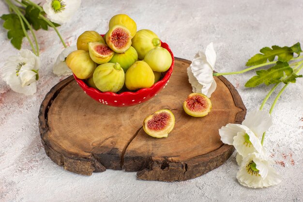 Vue avant de délicieuses figues sucrées fraîches à l'intérieur de la plaque rouge avec des fleurs sur un bureau blanc