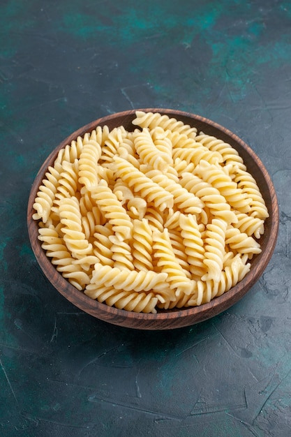 Vue avant de délicieuses pâtes italiennes à l'intérieur du pot brun sur le bureau bleu foncé
