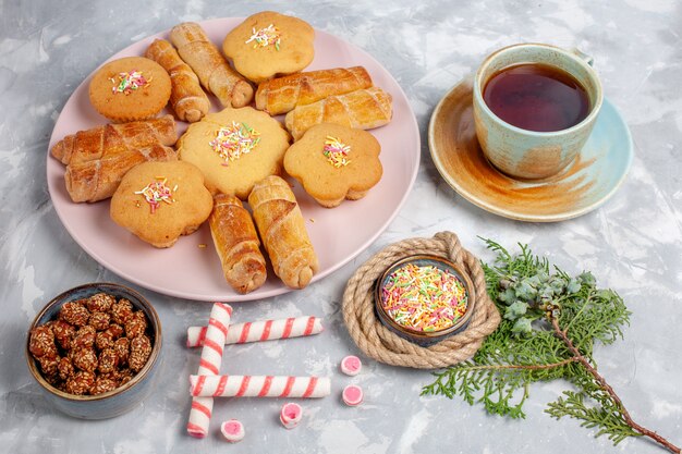 Vue avant de délicieux bagels avec des gâteaux et une tasse de thé sur un bureau blanc