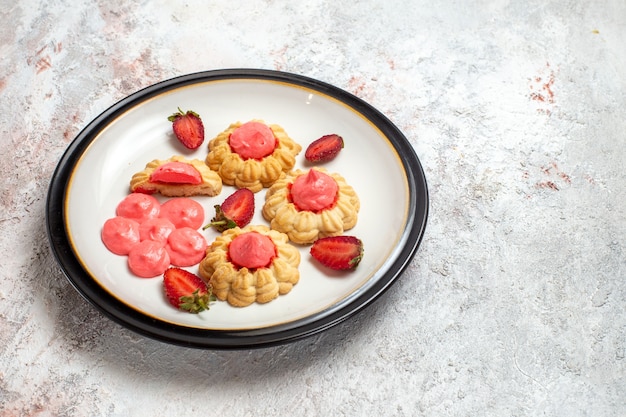 Vue avant de délicieux biscuits au sucre avec de la gelée de fraise sur un bureau blanc