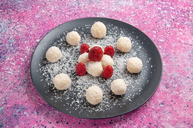 Vue avant de délicieux bonbons à la noix de coco boules sucrées sur mur rose