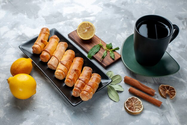 Vue avant de délicieux bracelets sucrés avec du citron cannelle et du thé sur table lumineuse, gâteau pâtisserie cuire le sucre sucré