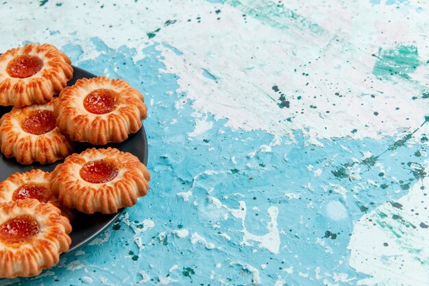 Vue avant de délicieux cookies avec de la confiture à l'intérieur de la plaque noire sur le mur bleu biscuit biscuit thé sucré couleur sucre