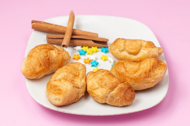 Vue avant de délicieux croissants cuits au four avec garniture de fruits à l'intérieur avec des bonbons à la cannelle sur le fond rose