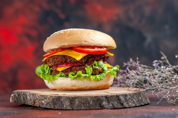 Vue avant de délicieux hamburger de viande avec du fromage et de la salade sur le fond sombre