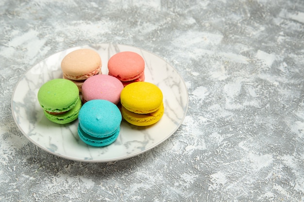 Vue avant de délicieux macarons français gâteaux colorés à l'intérieur de la plaque sur la surface blanche gâteau biscuit sucre biscuit tarte sucrée