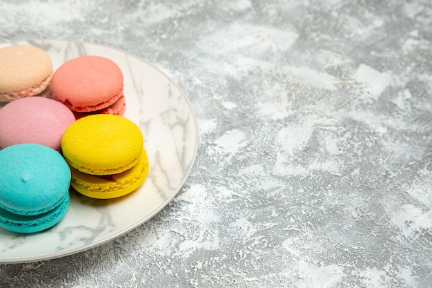 Photo gratuite vue avant de délicieux macarons français gâteaux colorés à l'intérieur de la plaque sur la surface blanche légère gâteau biscuit au sucre biscuits à tarte sucrée