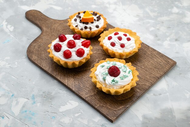 Vue avant de délicieux petits gâteaux à la crème et aux fruits sur la surface grise des fruits sucrés