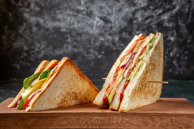 Vue avant de délicieux sandwichs au jambon sur une surface sombre de planche de bois