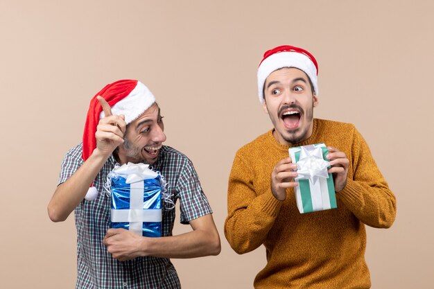 Vue avant deux gars ovejoyed rire et tenant des cadeaux de Noël sur fond isolé beige