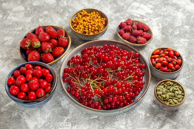 Vue avant différentes baies fraîches à l'intérieur des assiettes sur la table blanche de fruits frais de couleur berry