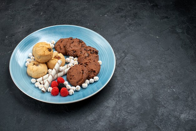 Vue avant différents cookies doux à l'intérieur de la plaque sur la surface grise biscuit sucre gâteau sucré cookie