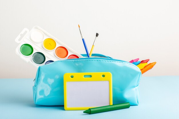 Vue avant de différents crayons et peintures colorés à l'intérieur de la boîte de stylo bleu sur le bureau bleu