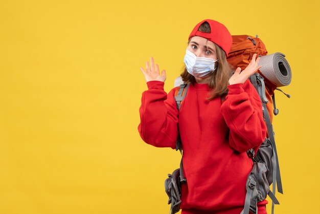 Vue avant du campeur féminin avec sac à dos et masque debout sur le mur jaune