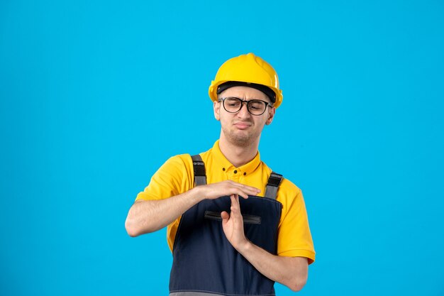 Vue avant du constructeur masculin mécontent en uniforme montrant le signe t sur un mur bleu