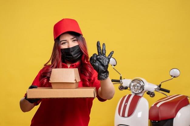 Vue avant du courrier féminin en masque avec livraison de nourriture sur mur jaune