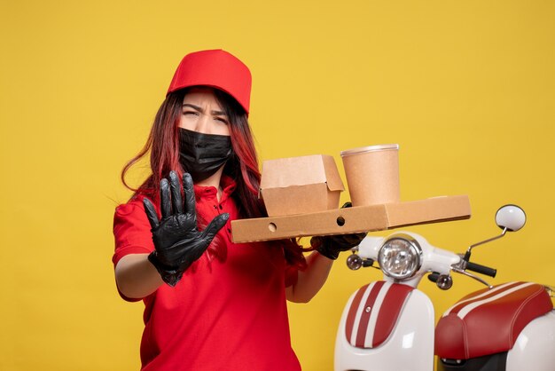 Vue avant du courrier féminin en masque avec livraison de nourriture sur mur jaune