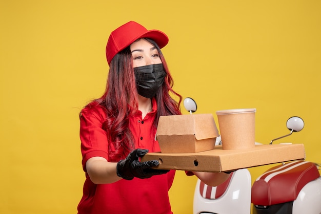 Vue avant du courrier féminin en masque avec livraison de nourriture sur mur jaune