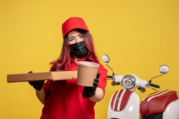 Vue avant du courrier féminin en masque avec livraison de nourriture sur mur jaune