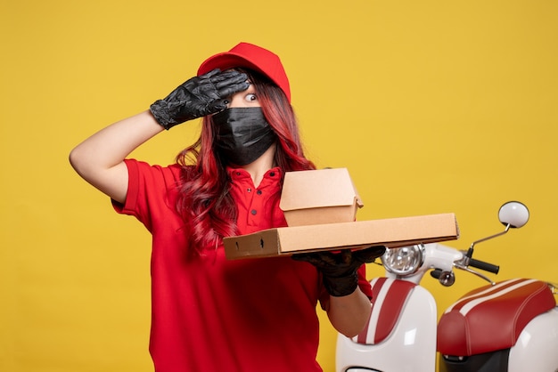 Vue avant du courrier féminin en masque avec livraison de nourriture sur mur jaune