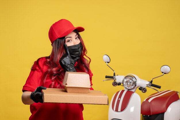 Vue avant du courrier féminin en masque avec livraison de nourriture sur mur jaune