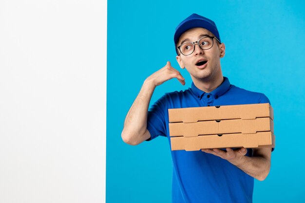 Vue avant du courrier masculin en uniforme bleu avec des boîtes de pizza sur un bleu