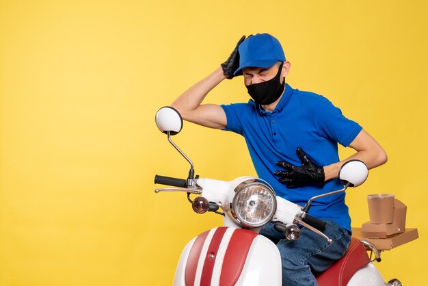 Vue avant du courrier masculin en uniforme bleu et masque ayant le chagrin sur le travail jaune covid- livraison virus de l'emploi de service de vélo pandémique