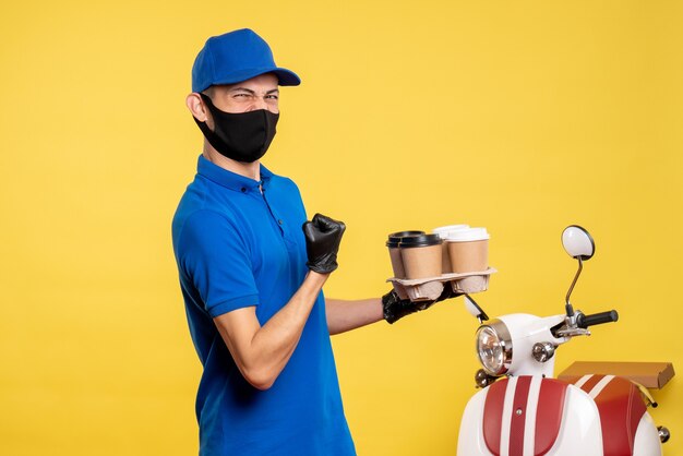 Vue avant du courrier masculin en uniforme bleu et masque tenant du café sur le service d'emploi jaune covid- pandémie de livraison de travail