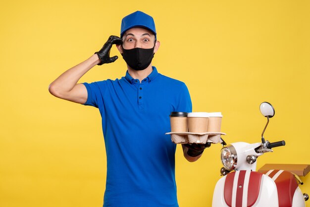 Vue avant du courrier masculin en uniforme bleu et masque tenant du café sur le service uniforme jaune covid- pandémie de livraison de travail