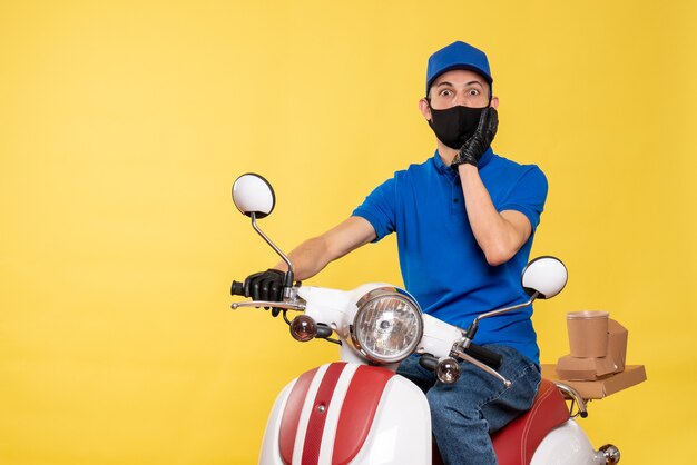 Vue avant du courrier masculin en uniforme bleu et masque sur vélo jaune travail pandémique covid- livraison de virus d'emploi