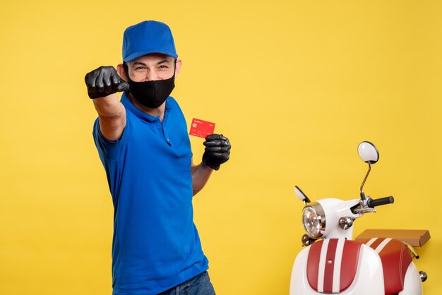 Vue avant du courrier masculin en uniforme bleu tenant la carte bancaire sur l'uniforme de service d'emploi jaune covid- travail couleur pandémique