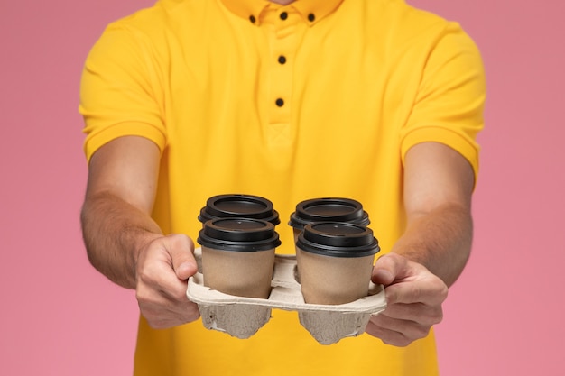 Vue avant du courrier masculin en uniforme jaune tenant des tasses de café de livraison marron sur le mur rose