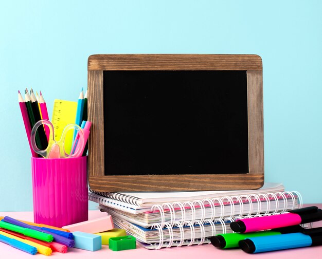 Vue avant du dos aux fournitures scolaires avec tableau noir et cahiers