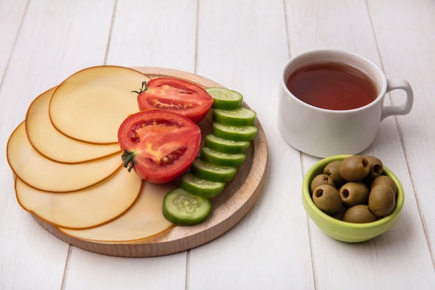 Vue avant du fromage fumé aux tomates concombres sur un support avec des olives et une tasse de thé sur fond blanc