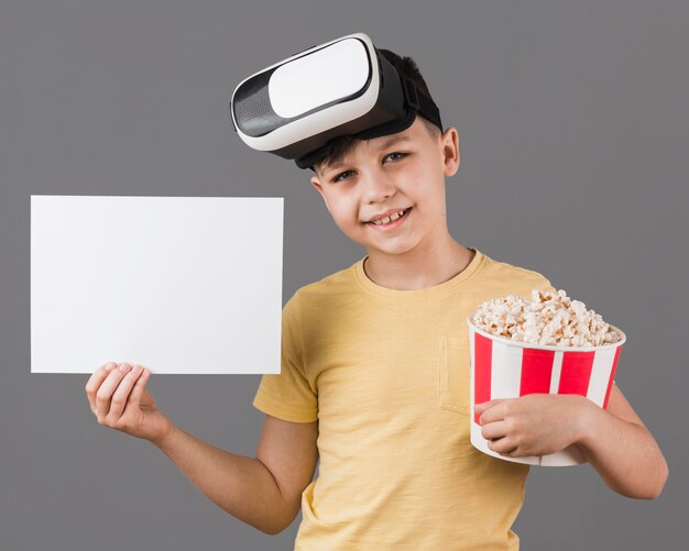 Vue avant du garçon avec un casque de réalité virtuelle tenant du pop-corn et du papier vierge