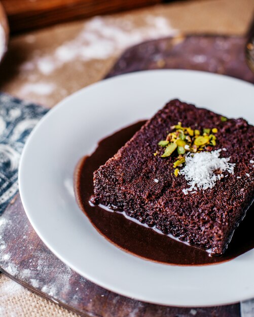 Vue avant du gâteau au chocolat savoureux doux à l'intérieur de la plaque blanche sur le bureau brun