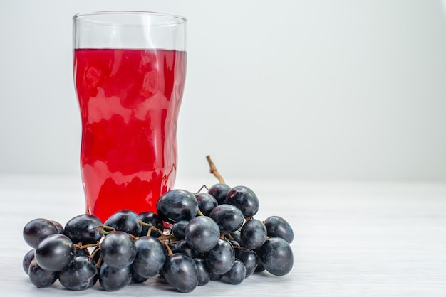 Vue avant du jus rouge avec des raisins sur la surface blanche du jus de cocktail boisson aux fruits