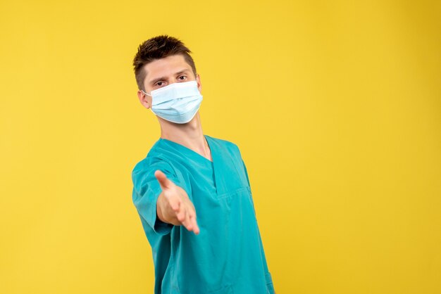 Vue avant du médecin de sexe masculin en costume médical avec masque stérile salutation sur mur jaune