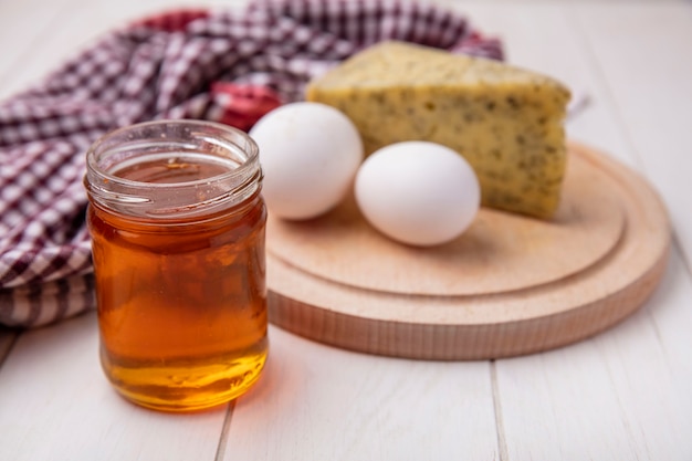 Vue avant du miel dans un pot avec du fromage et des œufs de poule sur un support sur un fond blanc